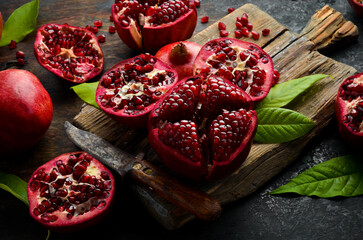 Ripe pomegranate fruit near leaf on dark wooden background. Free space for your text.