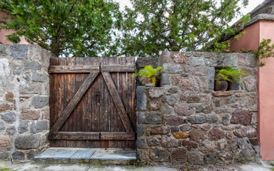 A natural wood door and low stonewall fence with trees and potted plants, Pachia Rahi village,...