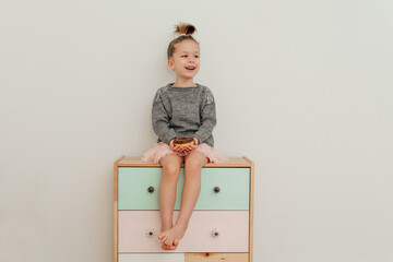 Funny little girl with modern hairstyle is sitting on the commode with chocolate donut. Portrait of...
