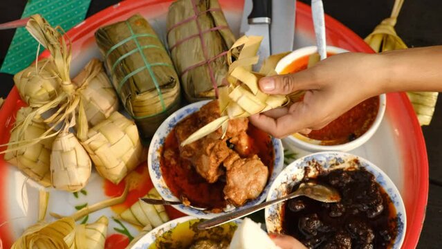 Top down handheld footage of hand taking ketupat with food insight "Hari Raya Aidilfitri". Famous traditional food ketupat, rendang, ayam masak merah and many more.