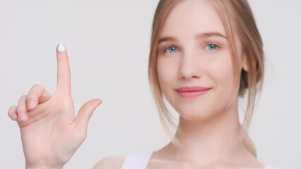 Young gorgeous beauty model shows a drop of cream on her finger. Demonstrates easiness of applying moisturizing cream | Skin care products advertising concept.
