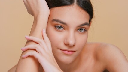 Close-up beauty portrait of young woman looks at camera and softly touches her hand skin, raises up her chin and smiles | Skincare products promotional concept
