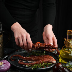 Cooked octopus tentacles with spices and herbs on a metal plate. Chef's hands in the frame. On a...