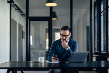 Serious male, reading something from his mobile phone, holding a hand on his chin.