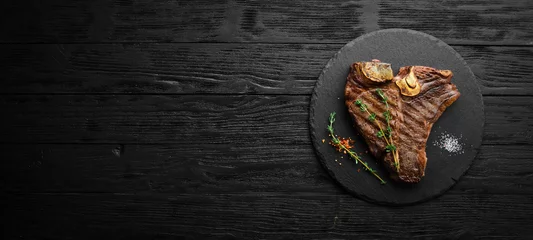 Poster Aged Beef T-Bone steak. Juicy cooked steak with rosemary and spices. Top view. Rustic style. Flat Lay. © Yaruniv-Studio