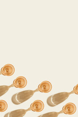 Wine glasses peach colored glass on beige background with shadow from sun. Summer light alcoholic drinks concept. Trendy wine goblets glasses, summer wine list backdrop, empty space