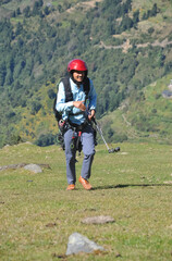 A excited Indian young male traveler smiling walking up in the mountain after finished paragliding flight