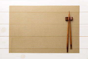 Two chopsticks and bamboo mat on wooden background. Top view, copy space