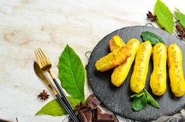 Eclair with mango cream. Mango dessert on a black stone plate. Top view. Rustic style.
