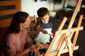 Mother and son painting at home. Little boy drawing with mom in living room