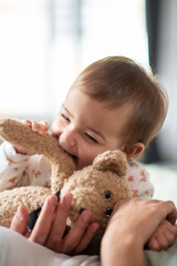 Portrait of happy baby boy biting his teddy bear. Cute little child playing with toy in bed. Childcare concept