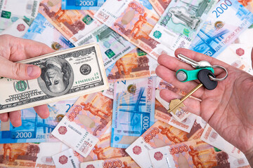 A hand with a bundle of US dollars and a hand with keys on the background of Russian money