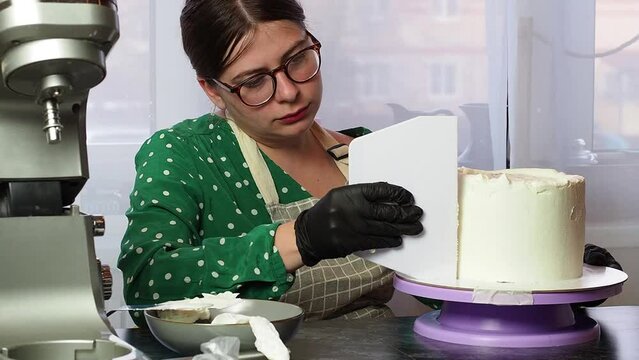 beautiful young confectioner girl makes a cake with white cream using a cooking spatula.