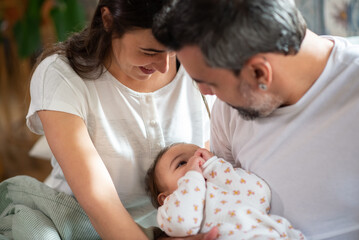 Happy loving couple holding baby son and looking at him. Mid adult parents sitting with little child in bed and smiling. Family at home concept