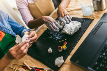 Mother and daughter spend time together and sculpting from clay at home watching online lessons