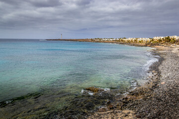 Playa de Montana Roja, Playa Blanca, Lanzarote. The picture also includes in the distance the Faro de Punta Pechiguera Antiguo, lighthouse