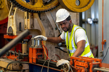African American industrial worker is using hydraulic power press machine to make metal and steel...