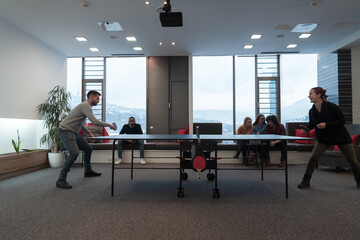 Young start up business man and woman playing table tennis at modern creative office space people group have meeting and brainstorming in background
