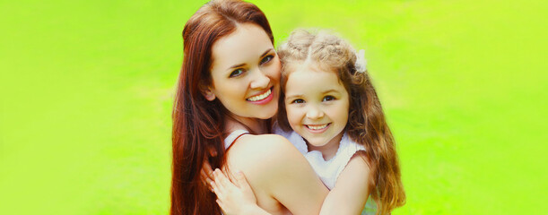 Portrait of happy smiling mother with little girl child on the grass in summer park