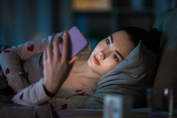 technology, bedtime and rest concept - teenage girl in pajamas with smartphone lying in bed at night