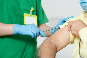 Close-up image of nurse in rubber gloves wiping shoulder of patient with cotton ball before injecting vaccine