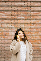 Portrait of a young woman, having a conversation on a phone, against a brick wall