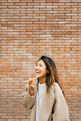 Fototapeta na wymiar Portrait of a young woman, using a phone, against a brick wall