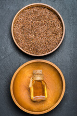 Glass bottle with linseed oil and flax seeds in a wooden bowl.