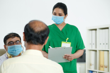 Medical nurse taking notes in document while physician talking to senior patient