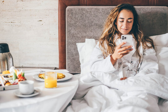 Woman eating breakfast and using phone in the hotel room. Room service breakfast in hotel room.