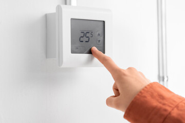 heating, energy and power consumption concept - close up of hand setting room temperature on...
