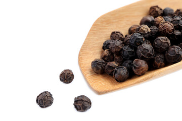 Fototapeta premium Close up of black pepper corns in a wooden spoon and scattered on white background.