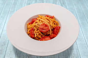 Italian Bavette pasta with tomato sauce, parmesan and fresh cherry tomatoes in white plate on light blue wood table