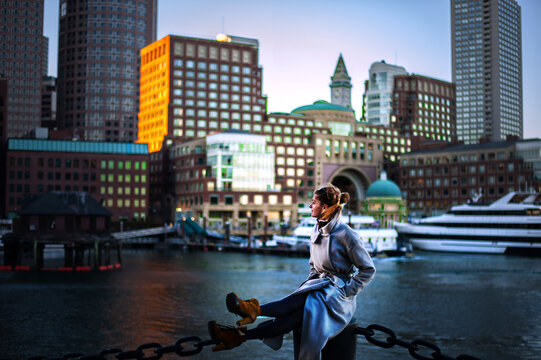 girl in coat against the backdrop of the cityscape yachts and riverboats moored in Boston harbor