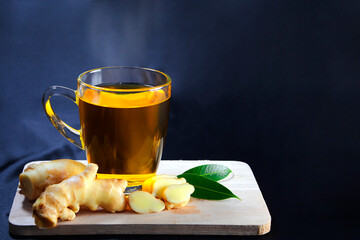 hot ginger juice in a glass Fresh ginger head and ginger slices placed on a wooden plank on black background with copy space text area.
