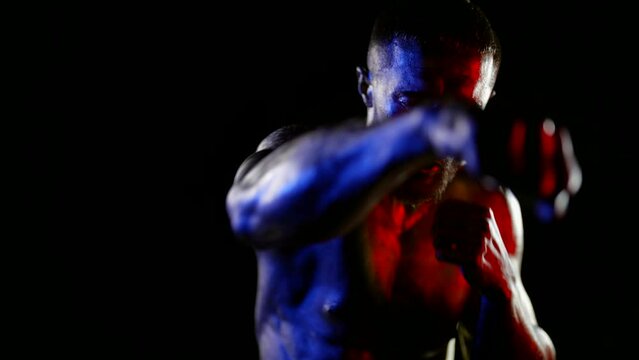 a muscular man with a bare torso and golden metallic skin is boxing against a dark background. front view. close-up. white, red and blue light