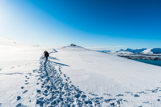 Tourists walking a hiking trail at the top of Storsteinen mountain in Tromso, Norway, on a sunny winter day