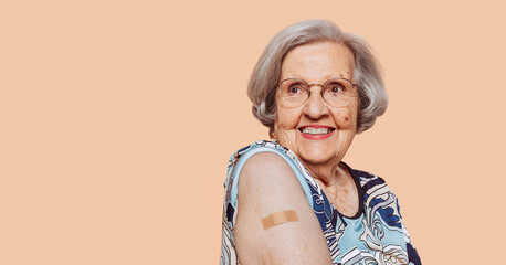 Portrait of a smiling elderly grandmother after receiving a vaccine. Elder woman showing her bandaged arm after receiving vaccination. - obrazy, fototapety, plakaty