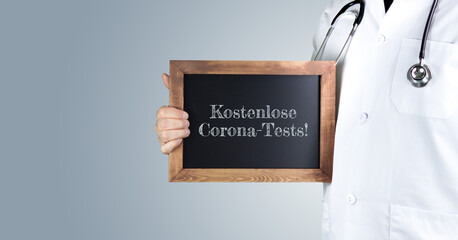 Kostenlose Corona-Tests!. Arzt zeigt Begriff auf einem Holz Schild. Handschrift auf Tafel