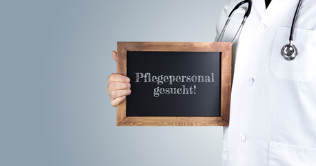 Pflegepersonal gesucht! (Arztpraxis). Arzt zeigt Begriff auf einem Holz Schild. Handschrift auf...