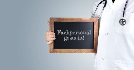 Fachpersonal gesucht! (Arztpraxis). Arzt zeigt Begriff auf einem Holz Schild. Handschrift auf Tafel