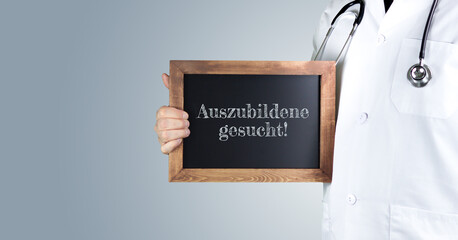 Auszubildene gesucht! (Arztpraxis). Arzt zeigt Begriff auf einem Holz Schild. Handschrift auf Tafel