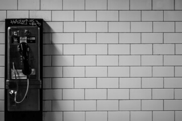 Black and white shot of a payphone a brick wall background - obrazy, fototapety, plakaty