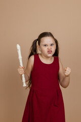 Girl in red dress with angry facial expression hold flute tightly in fist, beige background....