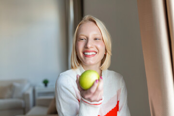 Young beautiful woman eating fresh apple and looking through window.