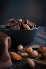 Raw choclate and choclate beans in black bowl with cocoa powder in the spoon - obrazy, fototapety, plakaty