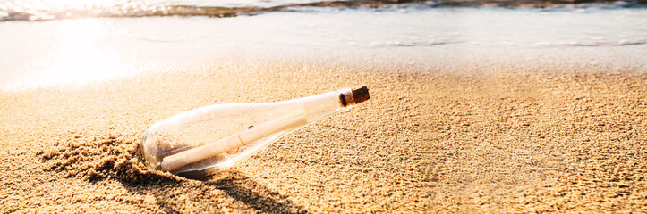 Message in a bottle on sand beach at sunset.
