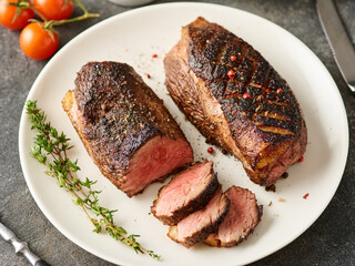Juicy tasty fragrant roasted duck breast on a white plate with peppers and cherry tomatoes.
