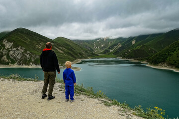 A man with a child on the background of Lake Kezenoy-am in the Caucasus mountains in Chechnya, Russia, June 2021.