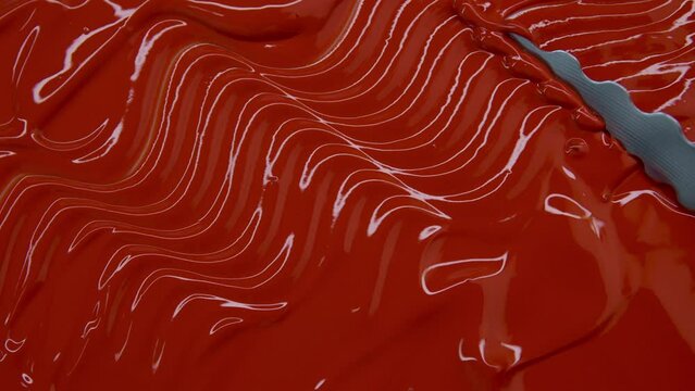 Red viscous glossy texture on a white background. Metal spatula smears red paint. Promotional concept for red lipstick or lip gloss. Decorative cosmetics for the face. Sample of red paint for artwork.